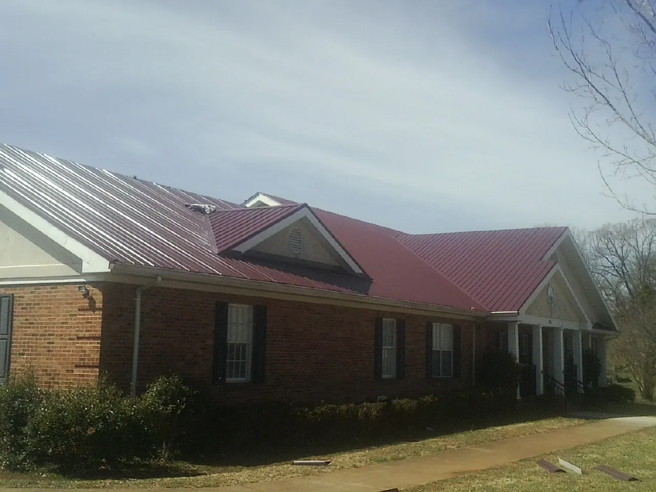 Red metal roof with gabled entries on a long brick building, from a Hail Damage Roof Repair job in Barnegat