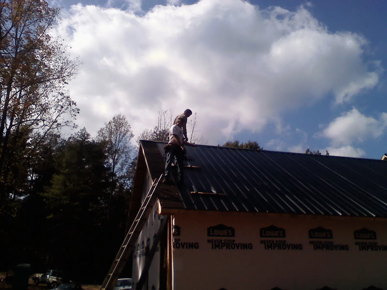 Roofer fastening dark metal panels high against a cloudy sky, from a Roof Inspection job in Barnegat