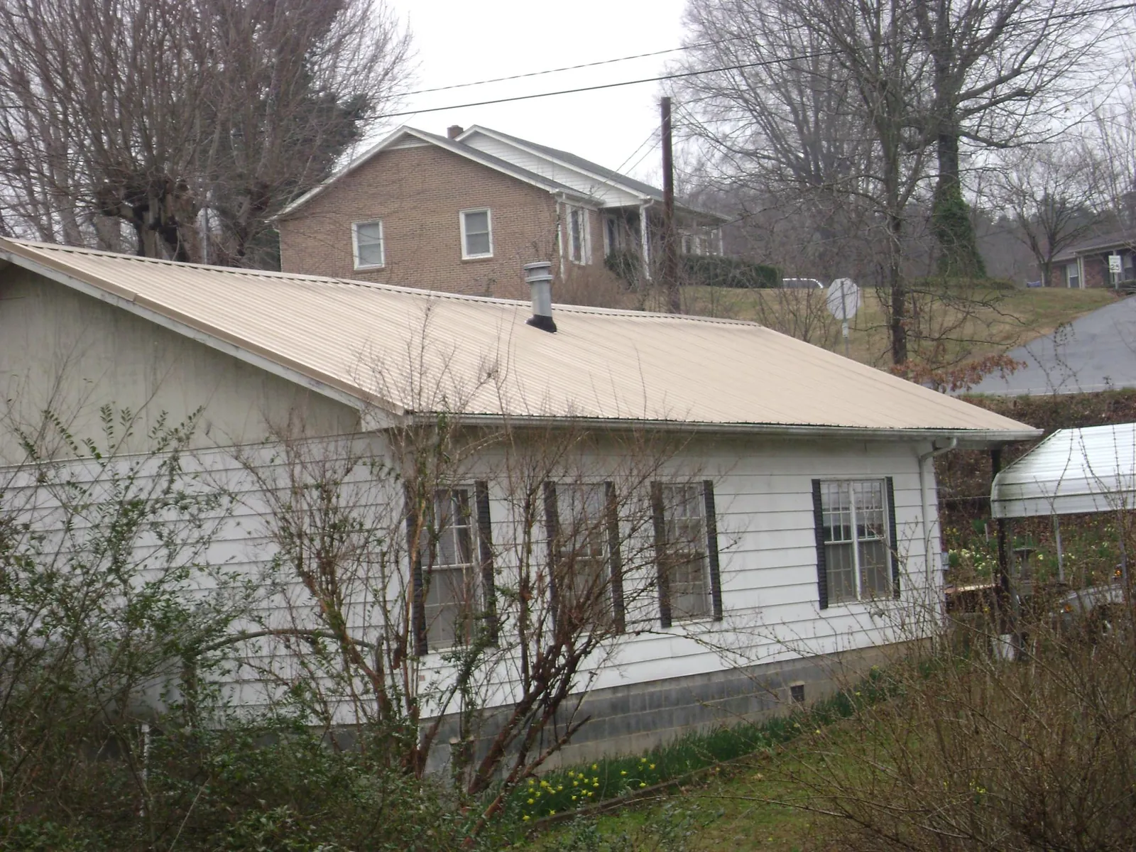 Tan metal roof on a white sided house set into a hillside — Commercial Roofing by Roofing Brothers in Barnegat